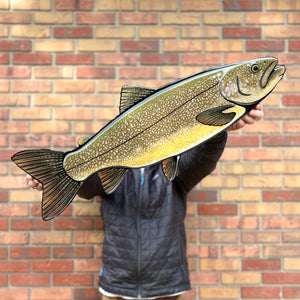 Person holding a large fish cutout against a brick wall